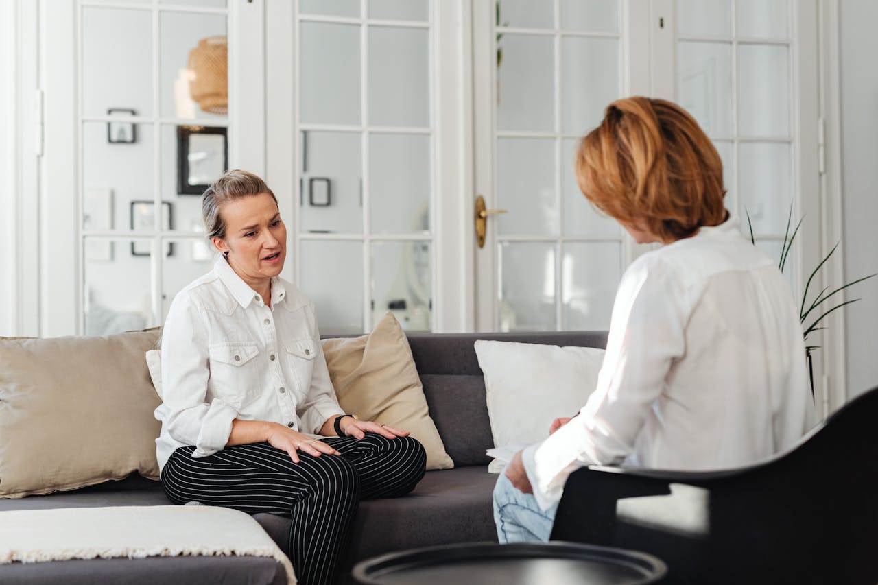 Two women having an intimate conversation on a sofa in a cozy indoor setting.